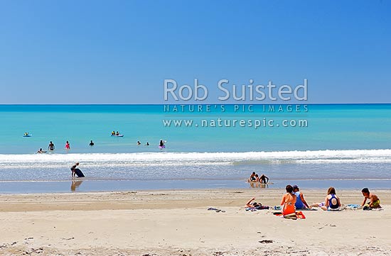 Families enjoying the summer on Waipiro Bay beach with azure blue water. Swimming, digging, sunbathing, kayaking and wave skis in surf, Waipiro Bay, East Coast, Gisborne District, Gisborne Region, New Zealand (NZ)