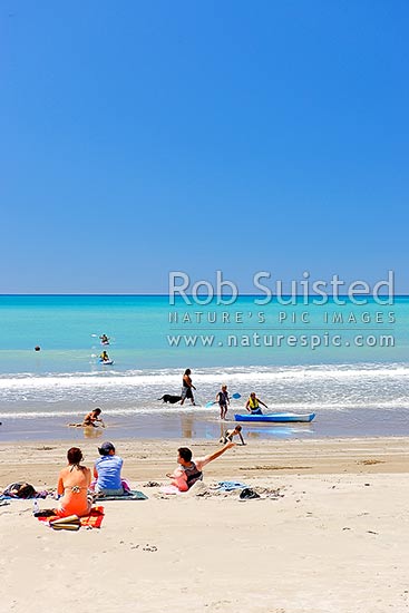 Families enjoying the summer on Waipiro Bay beach with azure blue water. Swimming, digging, sunbathing, kayaking and wave skis in surf, Waipiro Bay, East Coast, Gisborne District, Gisborne Region, New Zealand (NZ)