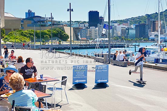 Wellington City waterfront with café diners enjoying meals near Chaffers Marina on a summer day. City skyline and te Papa Museum behind, Wellington, Wellington City District, Wellington Region, New Zealand (NZ)